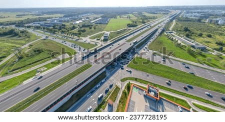 Aerial top view of highway junction interchange road. Drone view of the elevated road, traffic junctions, and green garden. Transport trucks and cars driving on highway. Infrastructure in modern city. Royalty-Free Stock Photo #2377728195