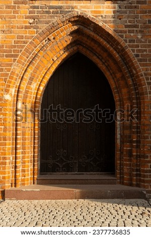 An antique wooden gate with forged metal patterns framed by brickwork. Vertical photo