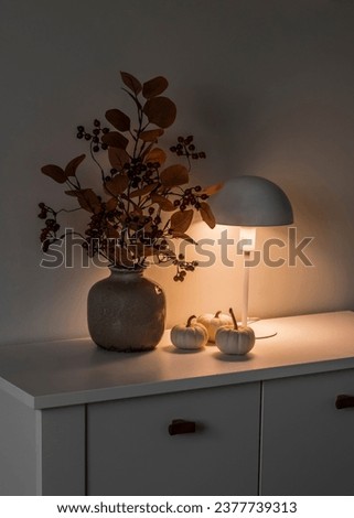 Autumn bouquet in a vase, pumpkins, a table lamp on the table in the evening living room Royalty-Free Stock Photo #2377739313