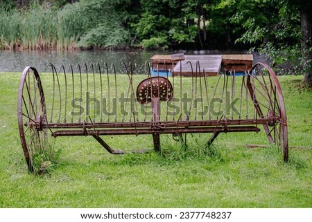 Old horse-drawn hay rake beside the pond 