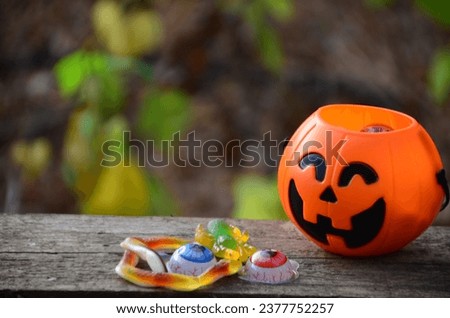 Halloween background. Spooky pumpkin i dark forest. Halloween design with copy space, concept. Various halloween sweets in a pumpkin pot on dark. Halloween party greeting card, eyes spiders snakes