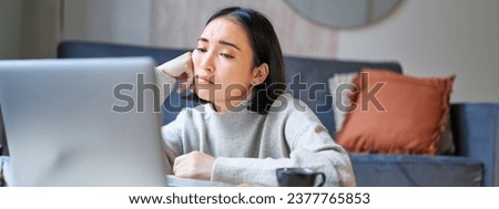 Portrait of korean girl sits bored, student looks gloomy at laptop, sitting at home and expressing boredom. Royalty-Free Stock Photo #2377765853