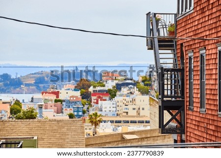 Side of reddish brown building with black stairs and patio overlooking city buildings in California