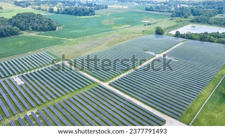 Solar panels facing straight up in aerial over solar farm with swamp and farmland around it Royalty-Free Stock Photo #2377791493