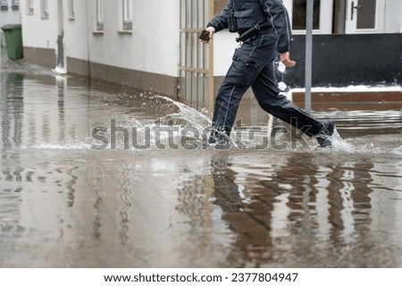 Policeman running through the water of a flooded street during high water of the river Trave in the old town of Lubeck at the Baltic sea in Germany, copy space, selected focus, motion blur Royalty-Free Stock Photo #2377804947