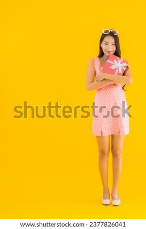 Portrait beautiful young asian woman with red gift box on yellow isolated background