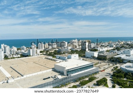 aerial shot of the Miami Beach Convention Center with blue ocean water and hotels and luxury condominiums in the city skyline, lush green palm trees, blue sky and clouds in Miami Beach Florida USA