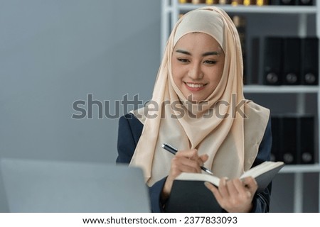Muslim woman lawyer wearing hijab asian, legal advisor, taking note and reading to legal code data on laptop. Business terms on books working with scales and hammers in office