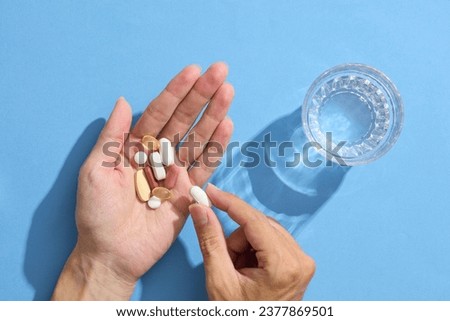Close up of a woman's hand holding multiple pills with a glass of water. Taking medication for headache relief, pain management, drinking water from the glass. The concept of healthcare, medicine. Royalty-Free Stock Photo #2377869501