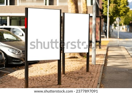 Two portrait format billboards between parked cars and sidewalk in Lugano Switzerland.