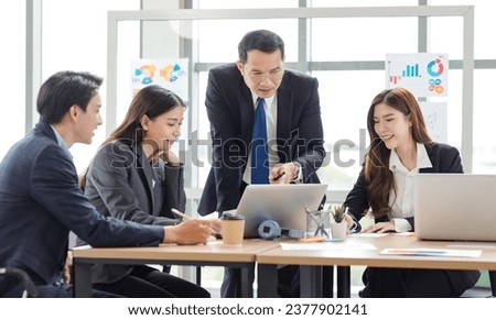 Asian professional successful businessman manager entrepreneur in formal suit standing teaching brainstorming marketing strategy with male female businesswomen employees team in company meeting room. Royalty-Free Stock Photo #2377902141