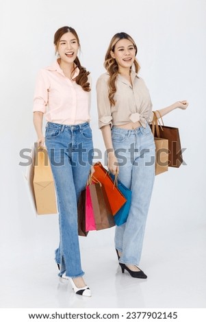 Portrait isolated cutout studio full body shot of two Asian cheerful female clients customers shoppers in casual outfit buying holding paper shopping bags in department store on white background.