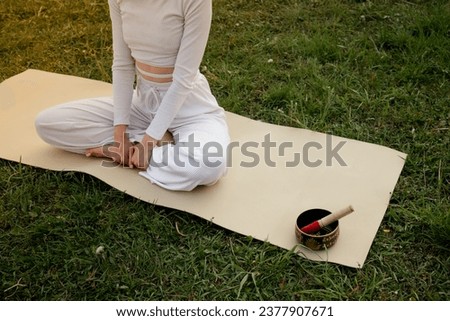 Female yoga training. Young girl in white sportswear sitting lotus caremat. Sports woman crossed legs peaceful retreat. Lady focused on chakra vitality. Spiritual wooden mortar.