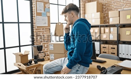 Young hispanic man ecommerce business worker sitting on table thinking at office