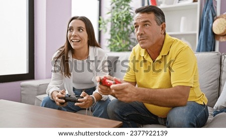 Hispanic father and daughter enjoy bonding time playing a video game at home, sitting on the living room sofa, smiles of joy on their faces, as they confidently use their gamepad controls.
