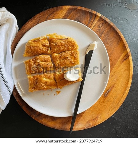 Filo pastry pie with squares on a plate, feta cheese Greek pie top view, mediterranean food picture, tiropita, wood platter, black background