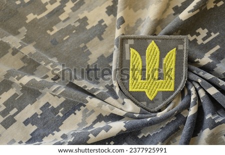 Symbol of Ukrainian army on the camouflage uniform of a Ukrainian soldier. The concept of war in Ukraine, patriotism and protecting your country from occupiers.