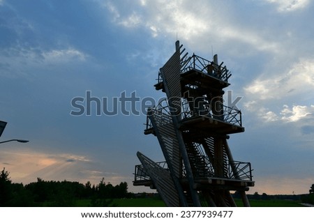A view of an unusual wooden tower made out of logs, planks, boards, and metal handles located next to a vast moor or forest seen on a cloudy evening right before a massive rainfall and storm Royalty-Free Stock Photo #2377939477