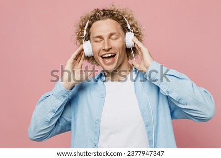 Young fun cheerful cool caucasian blond man wear blue shirt white t-shirt headphones listen to music dance close eyes isolated on plain pastel light pink background studio portrait. Lifestyle concept
