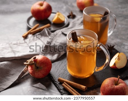Homemade apple punch with fresh apples, cinnamon and spices in cups on dark background with fresh fruits. A hot, healthy autumn or winter drink. The concept of a homely cozy atmosphere. Royalty-Free Stock Photo #2377950557