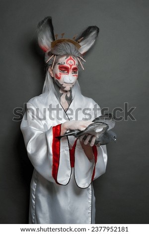 Rabbit woman with creative Halloween makeup hugging bird pigeon on blackboard background