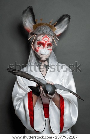 Young model woman with Halloween makeup holding bird pigeon on black background
