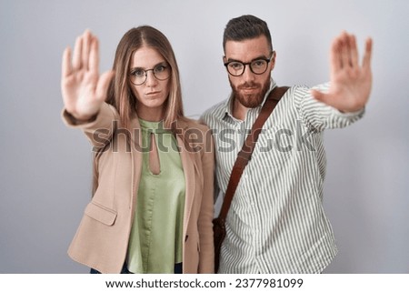 Young couple standing over white background doing stop sing with palm of the hand. warning expression with negative and serious gesture on the face. 