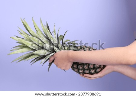 The Asian woman hand holding pineapple in the purple background.