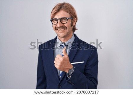 Caucasian man with mustache wearing business clothes doing happy thumbs up gesture with hand. approving expression looking at the camera showing success. 