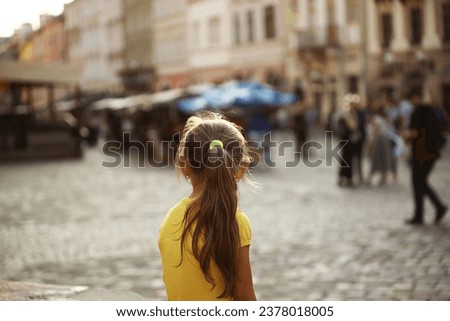 A little girl blonde looks into the distance standing on the street of a medieval European city. Little traveler. The city center of Lviv. Dreamy look to the future. Excursions and adventures in raisi