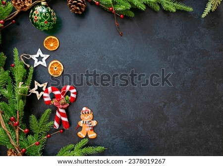 Vintage Christmas Background with, candy cane, gingerbread man, candied dried oranges, Christmas baubles, and wooden stars, a frame of a Christmas tree, with pine cones and berries, on grey slate 