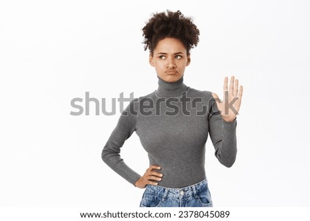 Portrait of woman looking away, pouting and showing stop gesture, disapprove and forbid action, standing in grey blouse over white background.