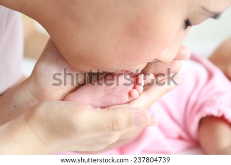 Asian mother playing with her infant baby lying on white bed background