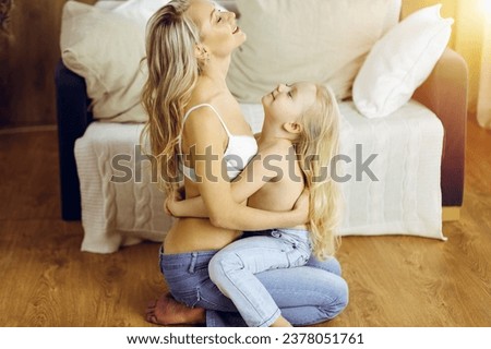 Happy mom and little daughter cuddle while dressing in sunny room. Motherhood and family concept