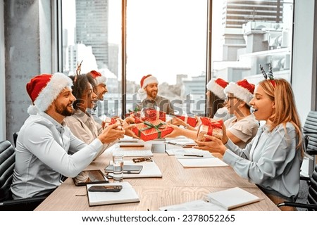 Christmas gift exchange at work. A group of happy business people are sitting at a table and exchanging gifts. Secret Santa.