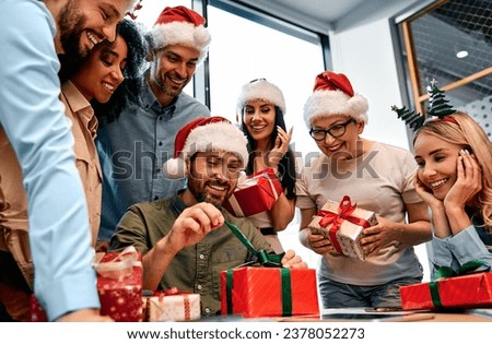 Secret Santa. A smiling man unpacks a Christmas present from colleagues at work. New Year's eve. Royalty-Free Stock Photo #2378052273