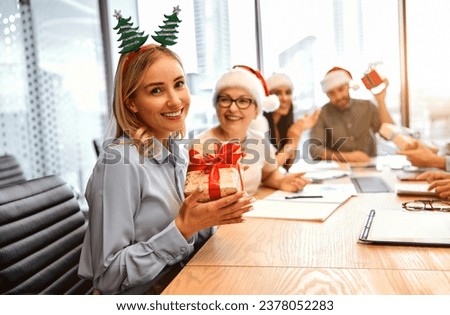 Receiving gifts at work is a pleasure. Adult beautiful happy smiling woman with ears with a Christmas tree holding a Christmas present and laughing looking at the camera.