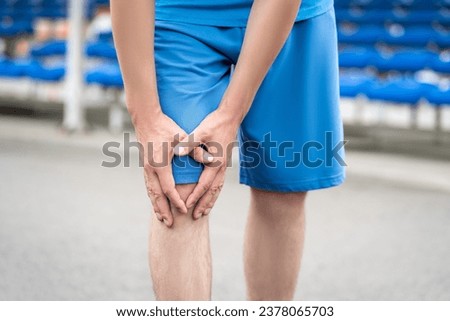 Diseases of the knee joint, bone fracture and inflammation, athletic man on a running track after workout suffering from pain in leg and doing self-massage, health problems concept