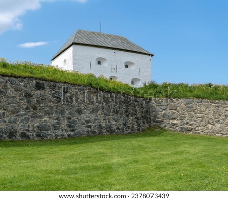 Kristiansten Fortress on top of the hill in the middle of Trondheim. Historical defensive structure from Norwegian past. Tower with lots of cannon holes. Cloudy summer day Royalty-Free Stock Photo #2378073439