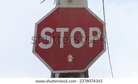 The image features a red stop sign with a white border mounted on a pole against a background of an overcast sky.