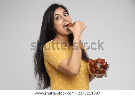 Indian young woman eating sweet Gulab Jamun on studio grey background