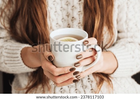 Hot tea in a mug. Woman holding mug of lemon tea. Cold winter relax background. Woolen sweater warm clothing. Long hair girl. Cozy atmosphere. Female hands holding tea. Royalty-Free Stock Photo #2378117103