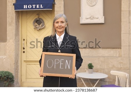 Happy business owner holding open sign near her hotel outdoors