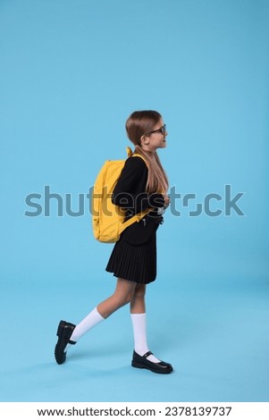 Happy schoolgirl with backpack on light blue background Royalty-Free Stock Photo #2378139737