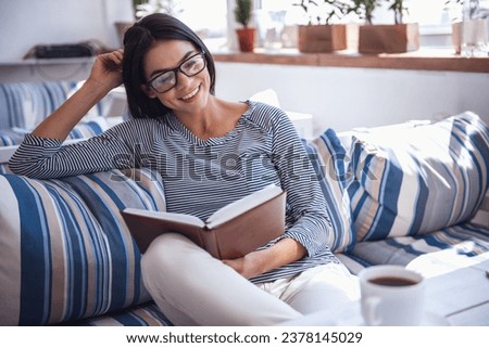 A young pretty girl sitting in a cafe drinking coffee and reading a book. Looks at the camera with a smile