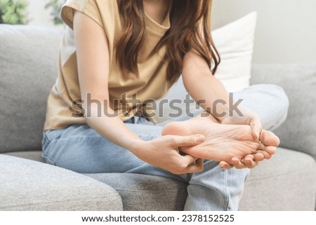 Foot pain concept, close up hand of young woman rubbing, massaging sore feet area of pain, girl suffering on sofa, couch at home. Discomfort painful feet ache from walking for long. Physical injury. Royalty-Free Stock Photo #2378152525