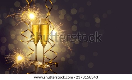 Two elegant perfect glasses filled with carbonated drink or sparkling champagne with golden serpentines and burning sparklers on  dark background. Christmas, New Year, anniversary