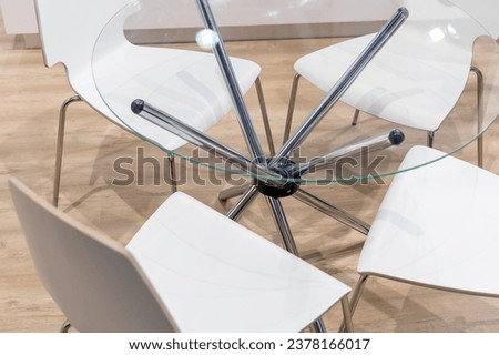 Glass table with metal chrome legs and white chairs around. Modern office furniture for communication between participants of corporate events or company employees