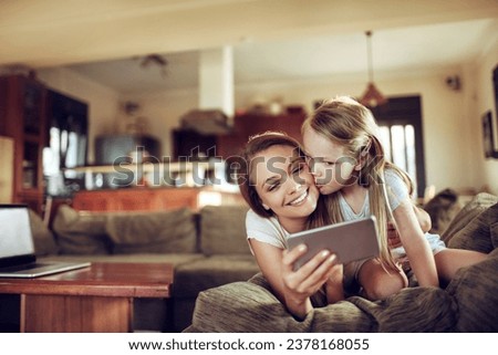 Happy little girl kissing her mother on the couch at home