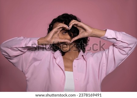 Cute studio valentines day shot of happy african american in pink shirt showing heart with her hands.